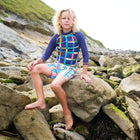 A boy sitting on rocks wearing UV Protective Swim Shorts Multi Stripe, rocks and hillside in background.